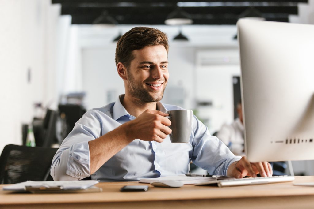 Smiling business man drinking coffee and using computer